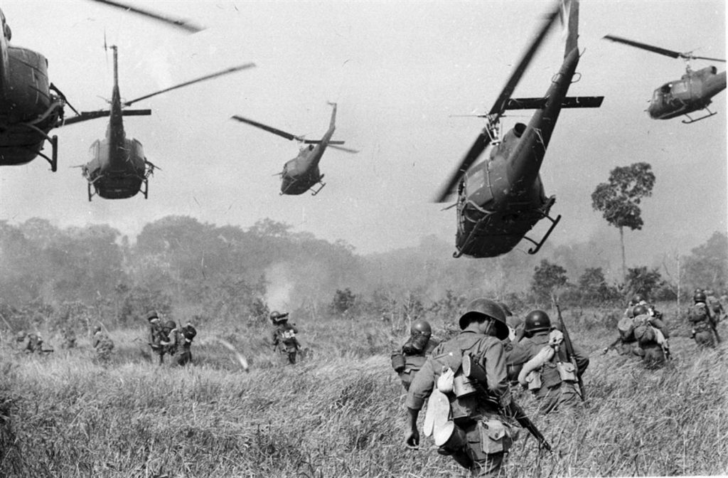 Helicopters hover over soldiers in a field during the Vietnam War.